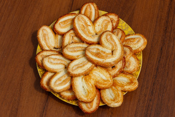Palmier biscuits - french cookies made of puff pastry (also called palm leaves, elephant ears or french hearts) in a plate on wooden table