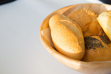 Close up of basket of various fresh bread rolls and buns on white table. Copy space or background for text or product presentation.