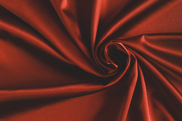 Close up of ripplesin shape of rose flower in red silk fabric. Satin textile background.