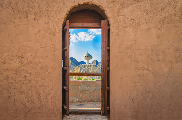 Narrow archway with old, heavy wooden doors opened to show the famous frankincense monument of Muscat, Oman. - obrazy, fototapety, plakaty