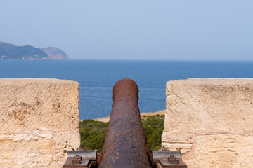 Fototapeta na wymiar Close-up of an old antique iron cannon on the old defence tower of Punta de N'Amer near Sa Coma, on the Spanish Balearic Mediterranean island of Mallorca
