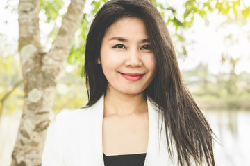 portrait of happy Asian working woman standing outdoor in a park smiling at camera 