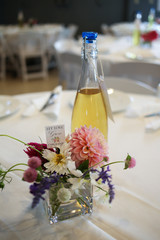 Rustic Wedding Centerpieces - Glass Bottle with Table Number Tag and Small Flower Arrangement of Pink, White, Fuchsia, Purple, and Green Flowers