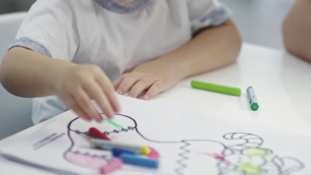 Close up of unrecognizable mother helping cute toddler girl coloring with crayons at table