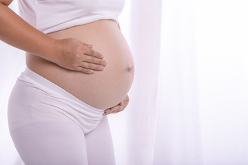 Young healthy pregnant in white clothes carefully holds her tummy - 7 months pregnant women on white curtain background.