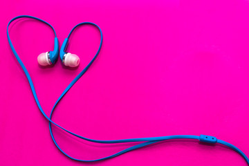 blue in ear headphones arranged in heart shape on purple background and copy space