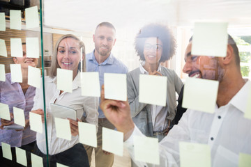 Group Of Businesspeople Sticking Adhesive Notes On Glass Wall