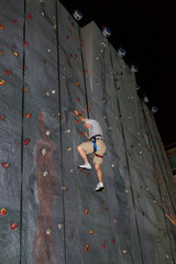 Elderly Man With White Hair and Casual Clothes Climbs an Outdoor Rock Gym Wall at an Amusement Park He is a Little More Than Half Way Up