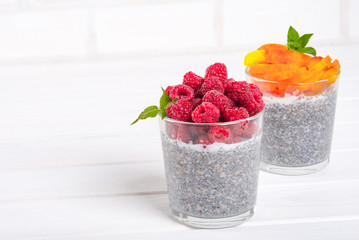 Food and drink, healthy eating and dieting concept. Homemade white chia pudding with fresh berries and green leaves for breakfast on a light kitchen table. Two glasses,peach or apricot and raspberry.