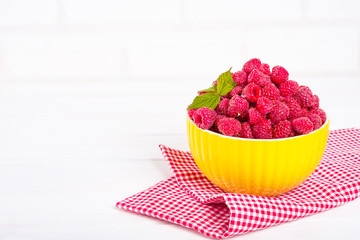 Fresh raspberry in a modern yellow bowl on light background
