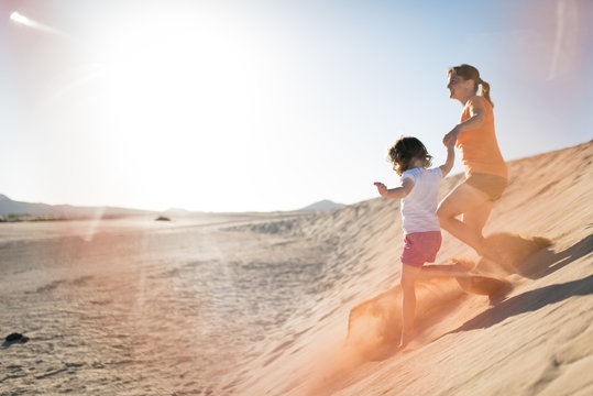 Mother and her little daughter running down the sand dune.