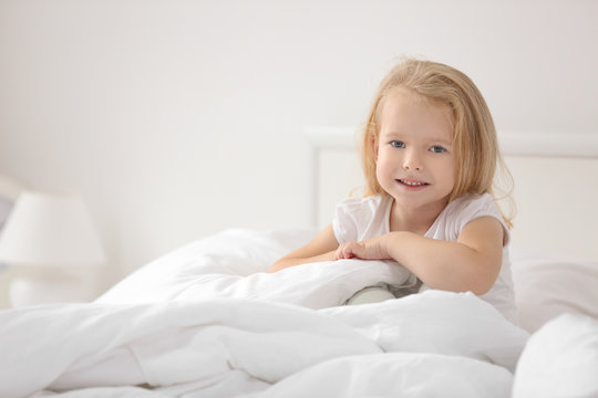 Little girl sitting on bed at home