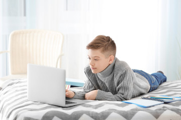 Teenager using laptop on bed at home