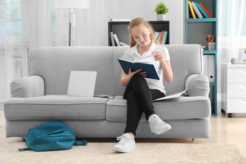 Teenage girl in school uniform reading book at home