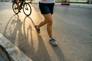 Obraz premium Close-up of sporty woman running on the road in the City park against a beautiful orange sunrise in early morning