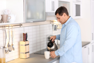 Handsome mature man making tea in kitchen