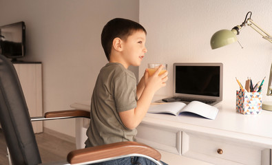 Cute little boy drinking tasty juice while doing homework indoors