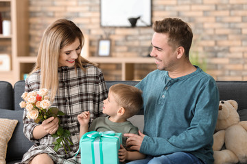 Happy woman receiving flowers and gift from husband and son at home