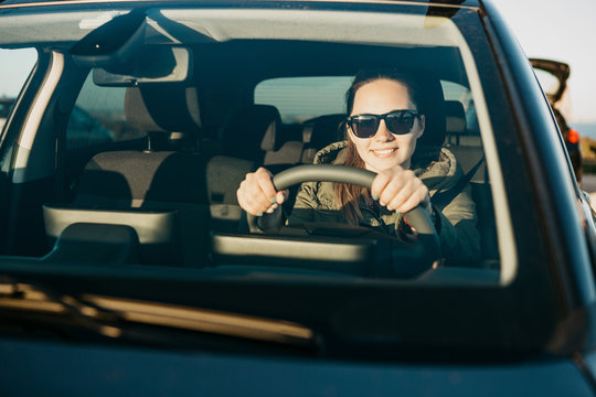 Portrait of a young smiling joyful woman or girl driver inside the car. Daily trips on transport or tourism, road travel or adventure.