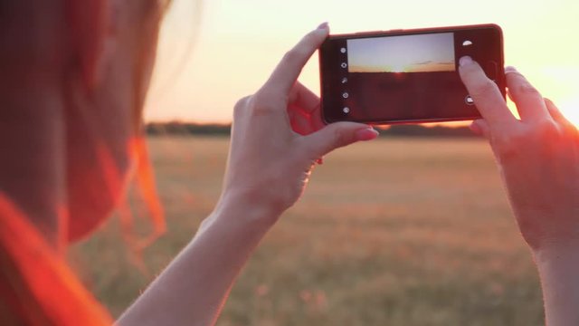 Close up of young woman taking photo of sunset on mobile phone