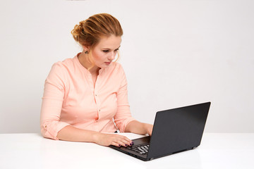 Portrait of a beautiful blond business girl on a white background sitting at the table with a laptop.