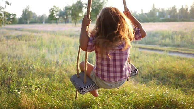 Happy cute little child girl have fun sway spin on a swing on nature sunset slow motion