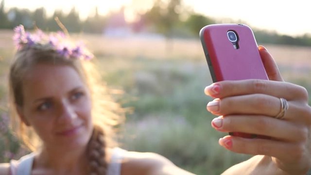 Make photo - young blonde lady taking selfie via smart phone on nature sunset