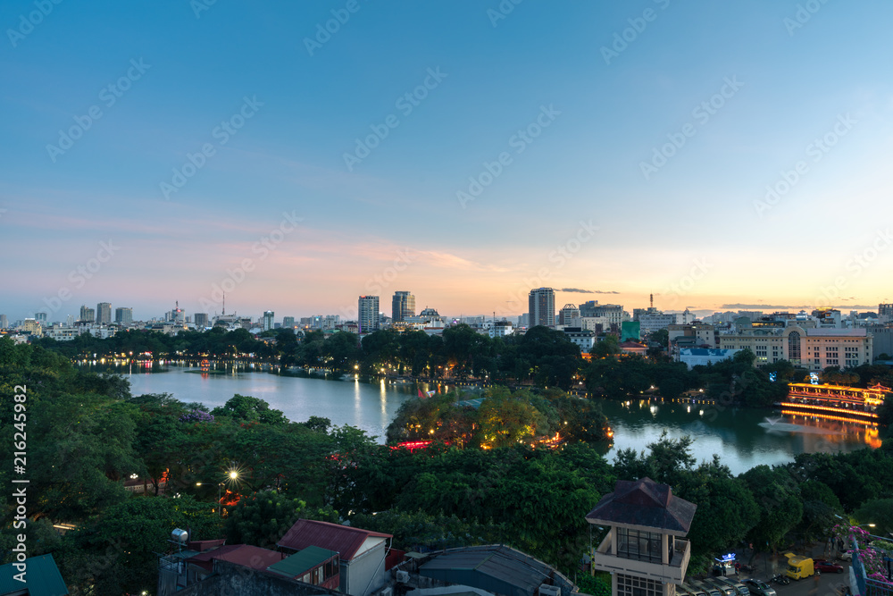 Wall mural Hoan Kiem lake or Sword lake, Ho Guom in Hanoi, Vietnam with Turtle Tower, green trees and buildings on horizon, at twilight period