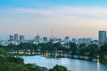Obraz premium Hoan Kiem lake or Sword lake, Ho Guom in Hanoi, Vietnam with Turtle Tower, green trees and buildings on horizon, at twilight period