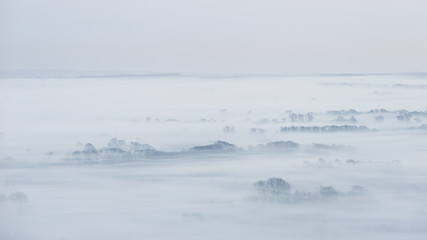 Stunning foggy English rural landscape at sunrise in Winter with layers rolling through the fields