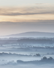 Stunning foggy English rural landscape at sunrise in Winter with layers rolling through the fields