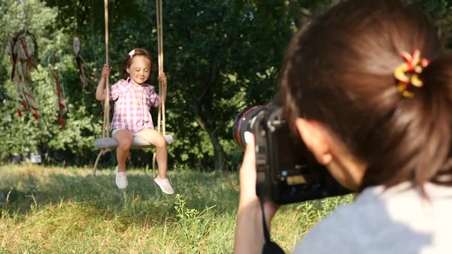 Woman photographer take photo shoot a little child girl sway on swing in nature