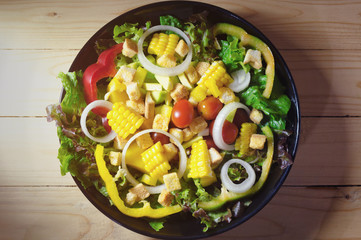 various fresh mix salad leaves with tomato in bowl on wooden background. with copy space. top view