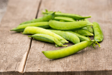 a scattering of fresh green peas pods from the garden on a wooden background