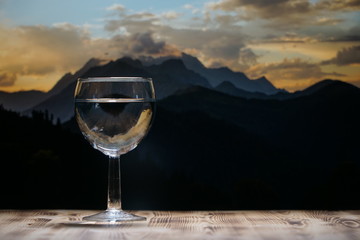 A glass glass glass with clean water stands on a wooden table against a mountain landscape.