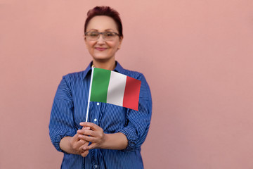 Italy  flag. Woman holding Italian flag. Nice portrait of middle aged lady 40 50 years old with a national flag over pink wall background outdoors. Learn Italian or visit Italy concept.