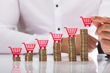 Businessperson placing shopping cart over stacked coins © Andrey Popov