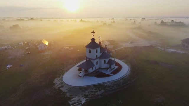 Aerial footage video of small village church at the foggy morning. Sunrise time. Kyiv region, Ukraine. Flying over the Desna river