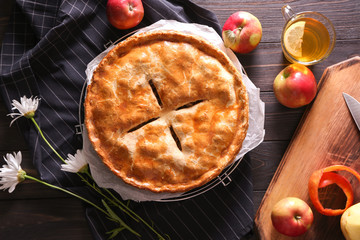 Cooling rack with delicious apple pie, flowers and cup of tea on wooden table