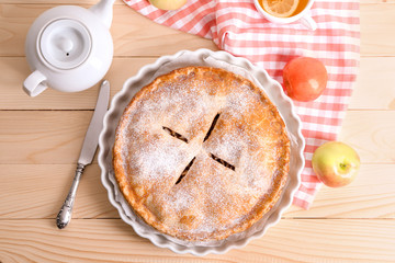 Plate with delicious apple pie and teapot on wooden table