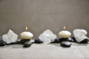 hydrangea petals with black stones and candle on gray background