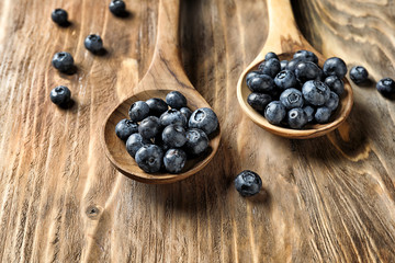 Spoons with ripe blueberries on wooden table, closeup