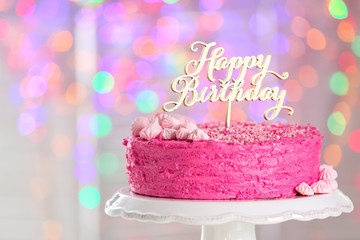 Stand with delicious birthday cake against blurred lights