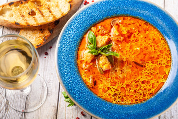 Italian European Cuisine. Spicy fish soup from seafood, salmon and trout, with vegetables in a blue plate. on the table in the restaurant is a glass of white wine. Copy space, selective focus