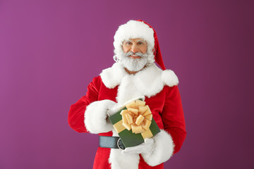 Santa Claus with gift box on color background