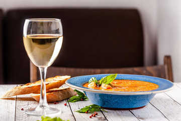 Italian European Cuisine. Spicy fish soup from seafood, salmon and trout, with vegetables in a blue plate. on the table in the restaurant is a glass of white wine. Copy space, selective focus
