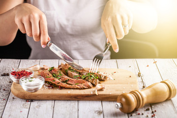 Mexican food. The girl has a fillet of meat steak with the addition of spicy green salsa. meat on a wooden board. Knife and fork in hands. concept of a beautiful dish in a restaurant. selective focus