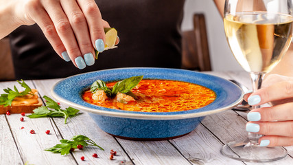Italian Cuisine. The girl at the restaurant eats fish soup from seafood and salmon, squeezes lime into the soup and drinks white wine. Copy space, selective focus