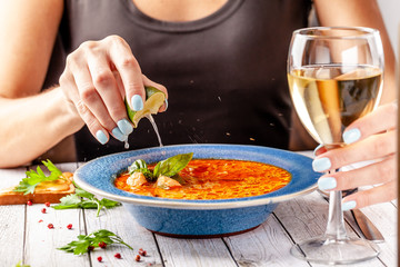 Italian Cuisine. The girl at the restaurant eats fish soup from seafood and salmon, squeezes lime into the soup and drinks white wine. Copy space, selective focus