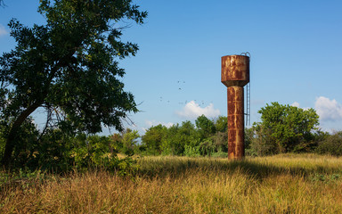 Old Rusty Industrial Water Tower in Village in Summer Morning